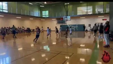 Kids playing basketball in a gymnasium, with spectators along the walls